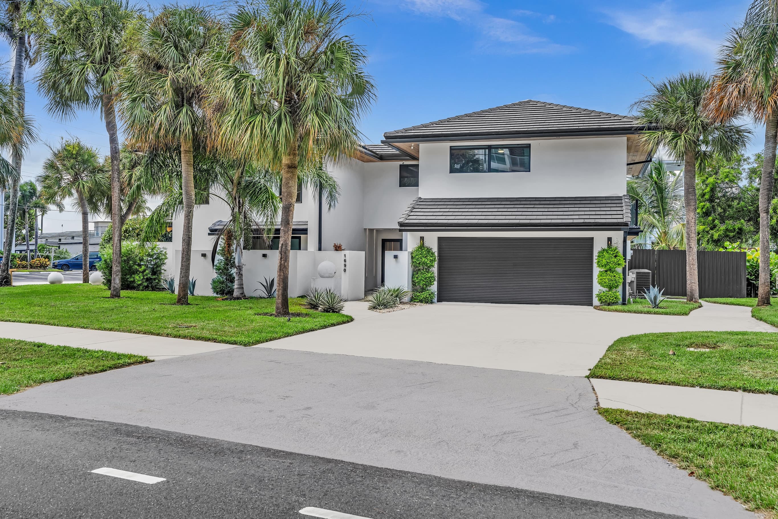 Modern white two-story home with a dark tile roof, a two-car garage and palm trees on a South Florida street